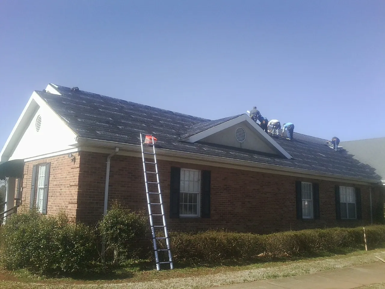 Crew tearing shingles off a brick ranch roof with a ladder set — Metal Roof Repair work by our crew in Martins Creek
