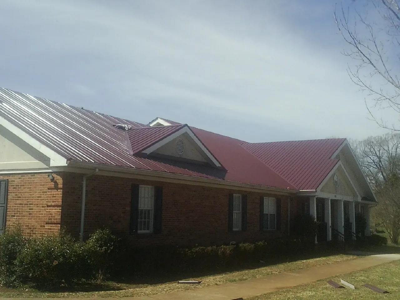 Red metal roof with gabled entries on a long brick building, from a Hail Damage Roof Repair job in Martins Creek