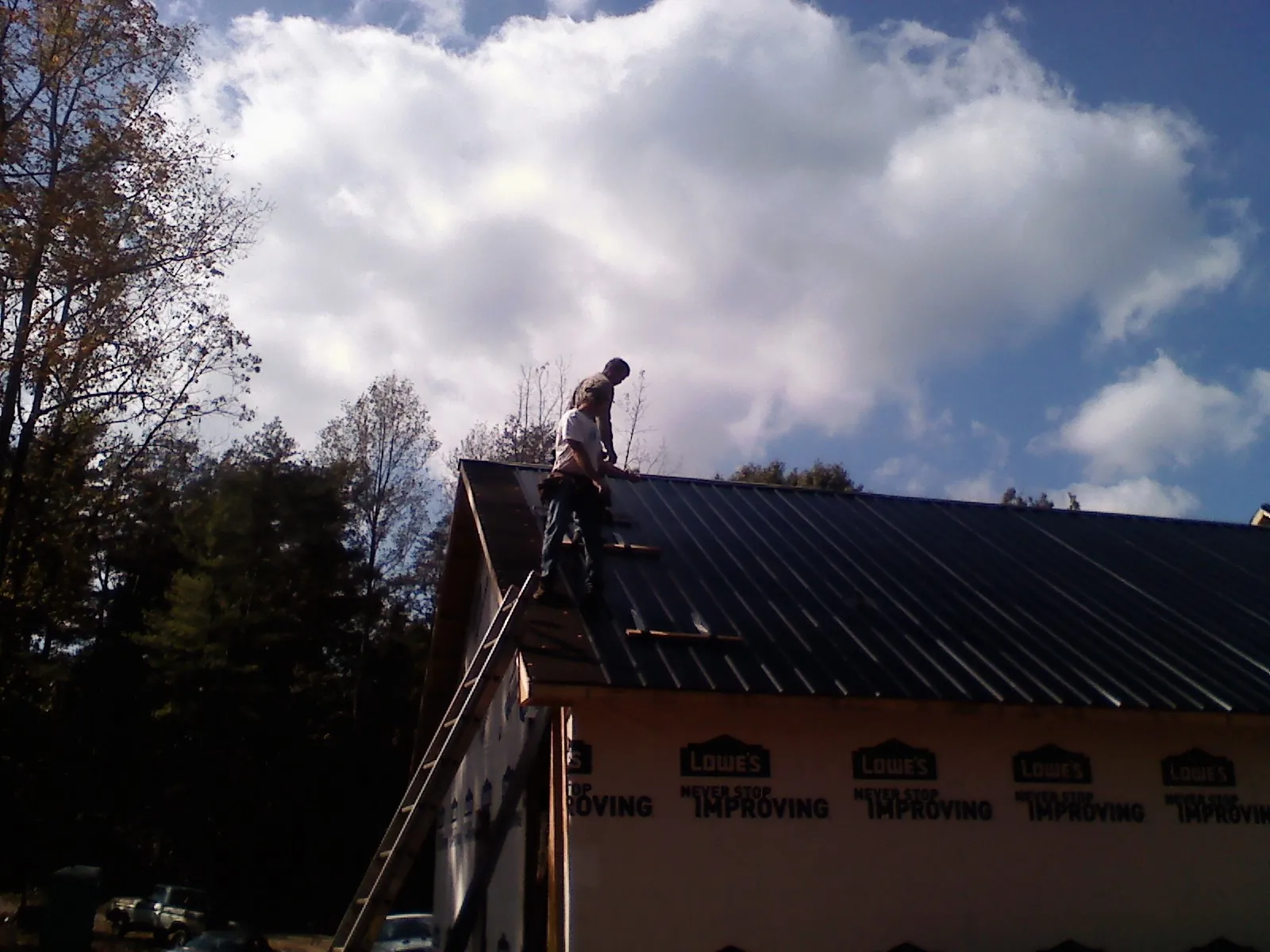 Roofer fastening dark metal panels high against a cloudy sky, from a Roof Inspection job in Martins Creek
