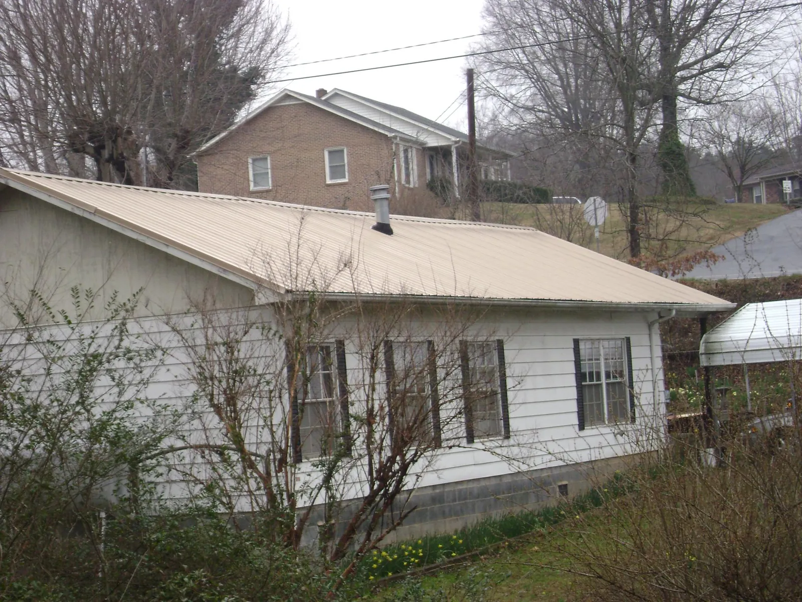 Tan metal roof on a white sided house set into a hillside — Commercial Roofing by Roofing Brothers in Martins Creek